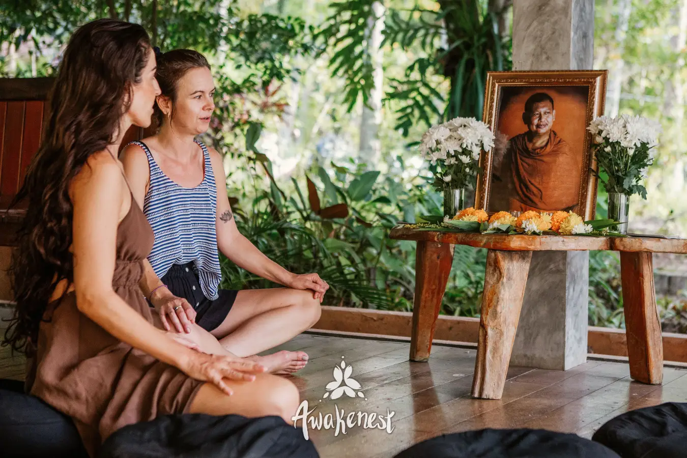Two women meditate again before monk portrait.