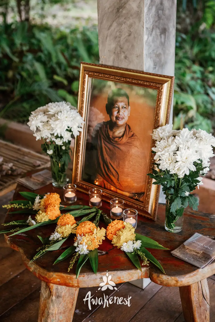 Framed monk portrait with candles and flowers.