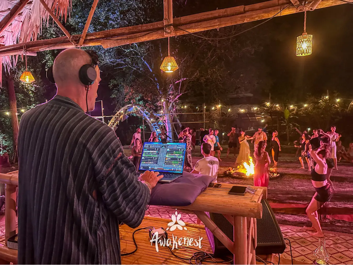DJ mixing for dancers around night fire.