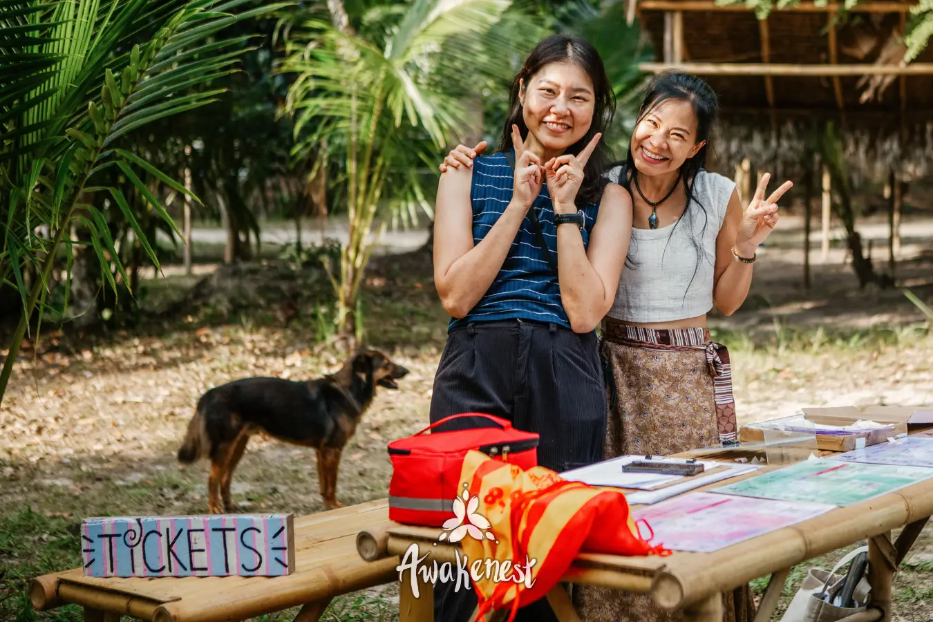 Two women pose smiling near ticket sign.
