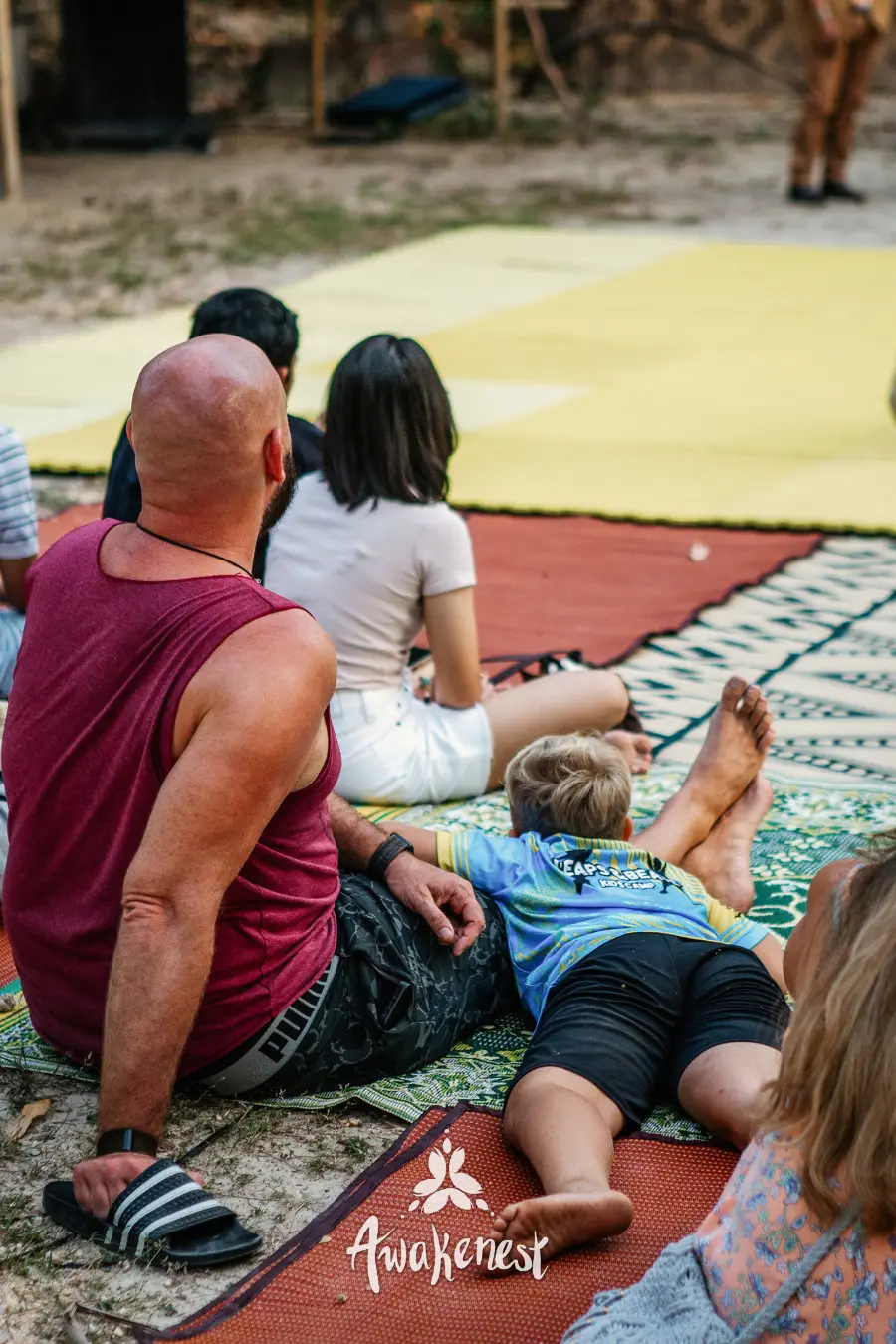 Family relaxing together on woven mat.