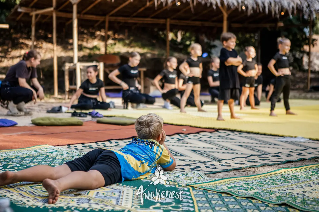 Child lies on mat watching dance rehearsal.