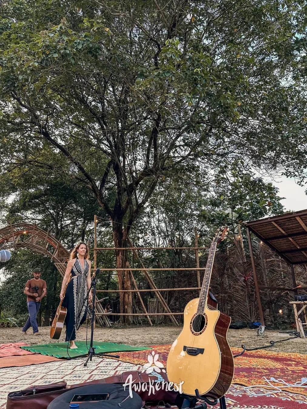 Woman sings at outdoor mic beside guitar.