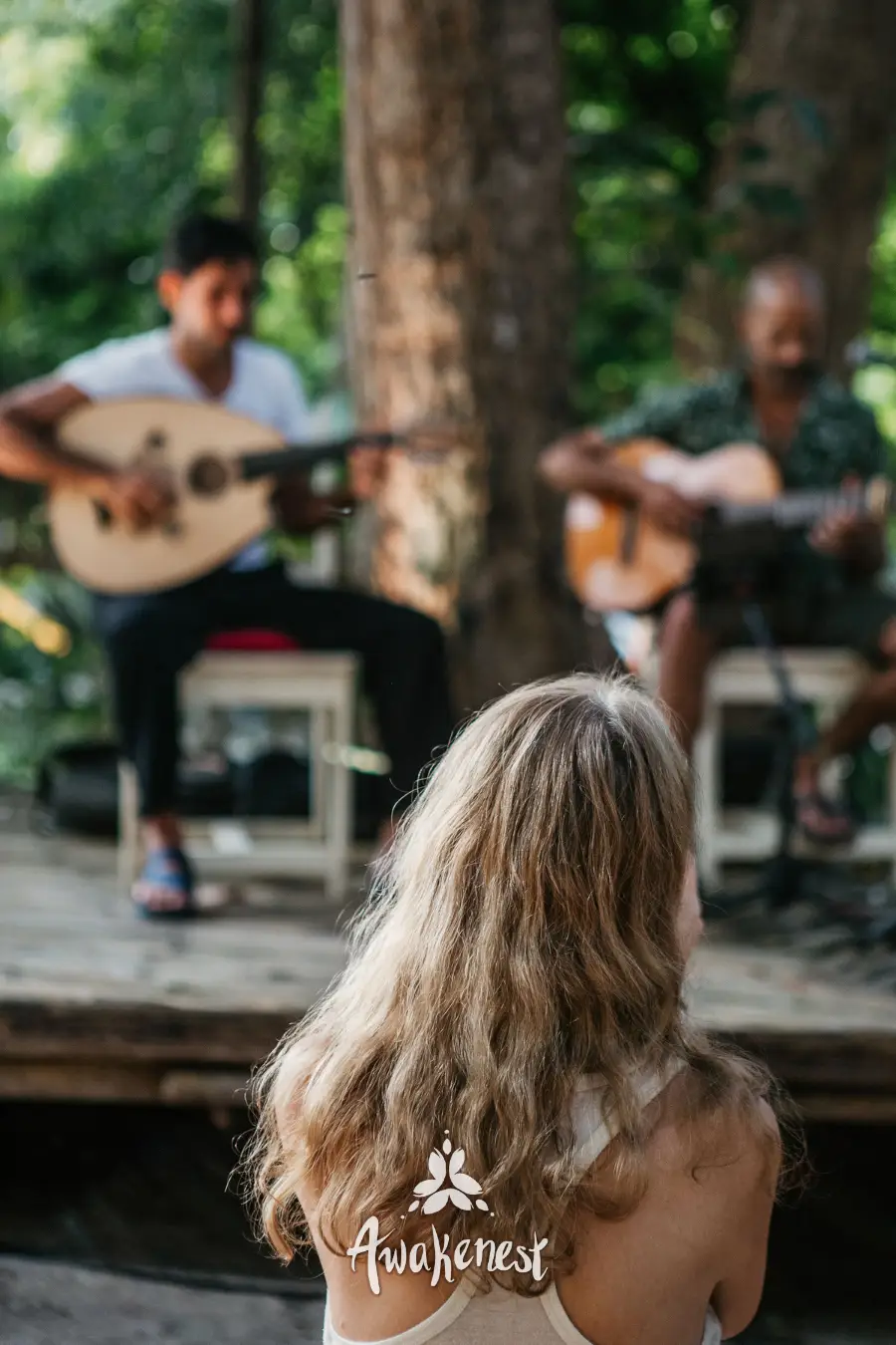 Guitar duo performing under trees for listener.
