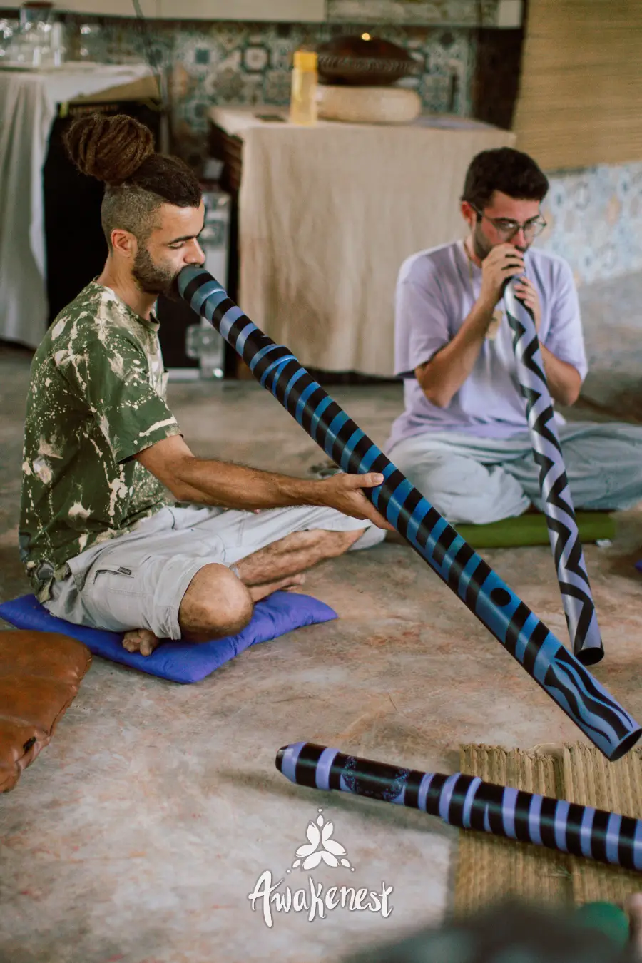 Two men playing didgeridoos seated indoors.