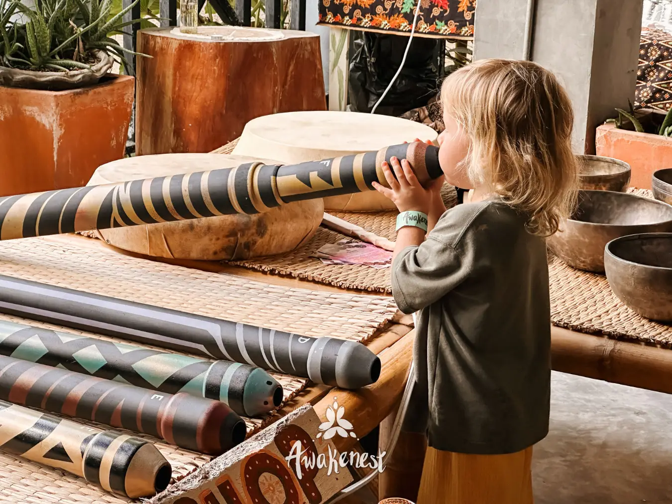 Child looks through didgeridoo at market stall.