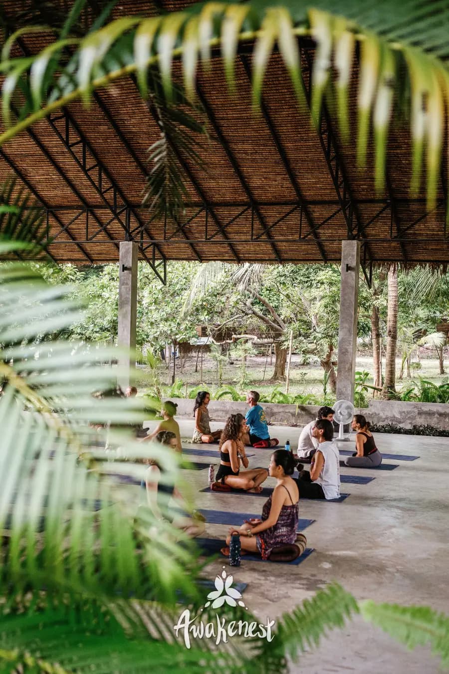 Group seated in circle under thatched pavilion.
