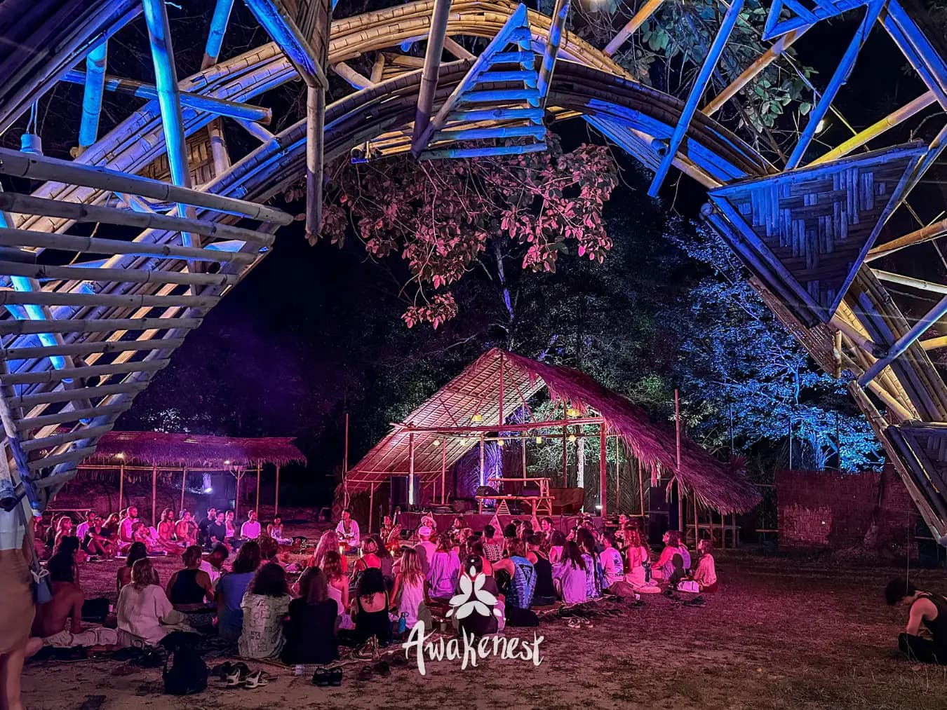 Crowd seated beneath lit bamboo dome at night.
