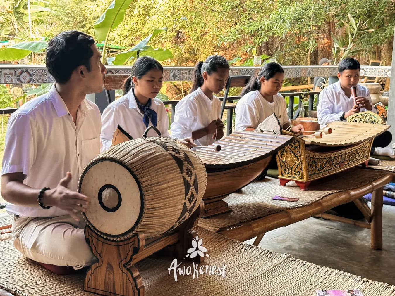 Young musicians in white play a Thai drum, two wooden xylophones and a flute on a bamboo platform.