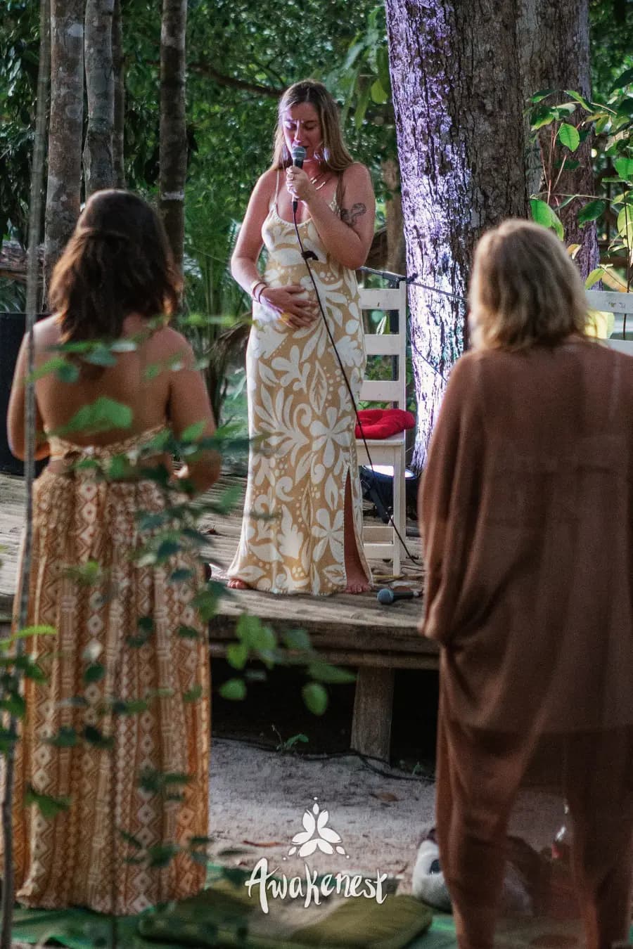 Woman speaking on outdoor stage in gown.