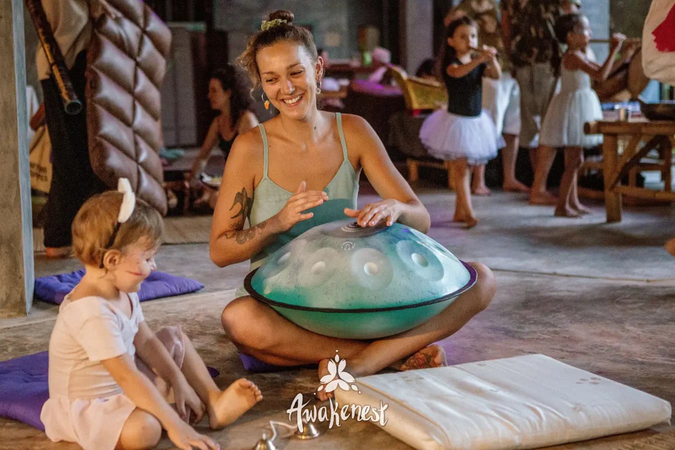 Woman plays handpan beside seated child.