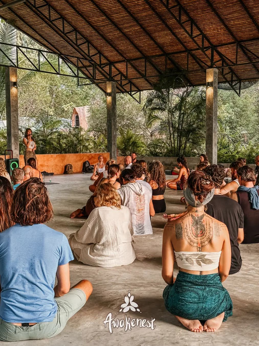 Large group circle facing facilitator under pavilion.