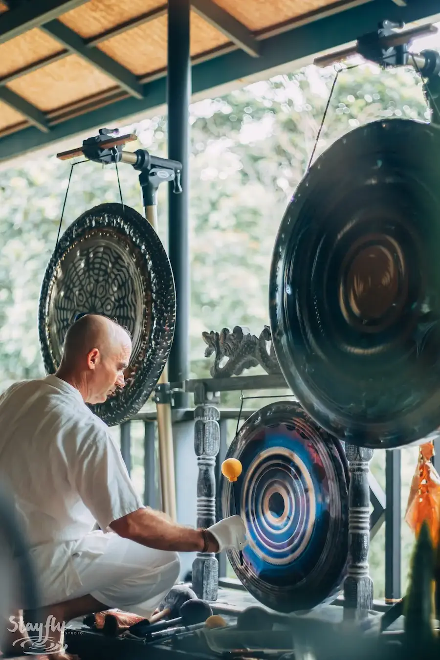 A practitioner in white plays a large gong hung at the pavilion railing.