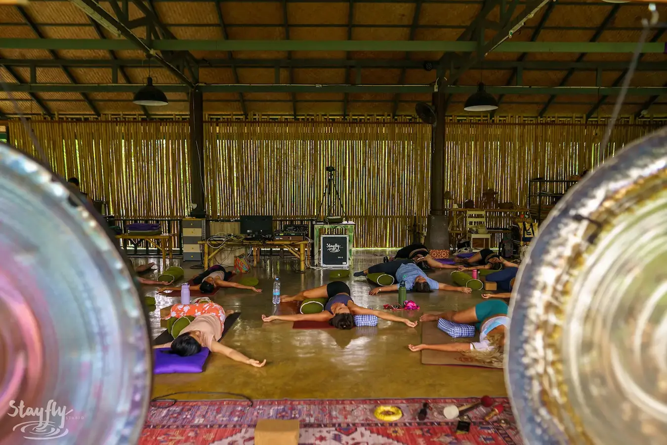 Two gongs seen close, with participants resting on the pavilion floor beyond them.