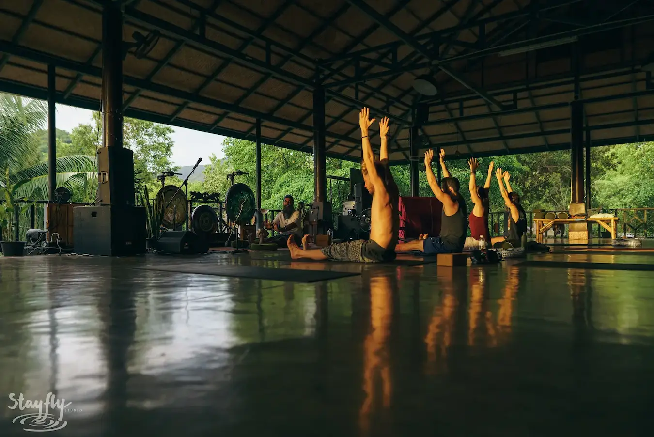 A yoga class holds a pose together in the pavilion by daylight.