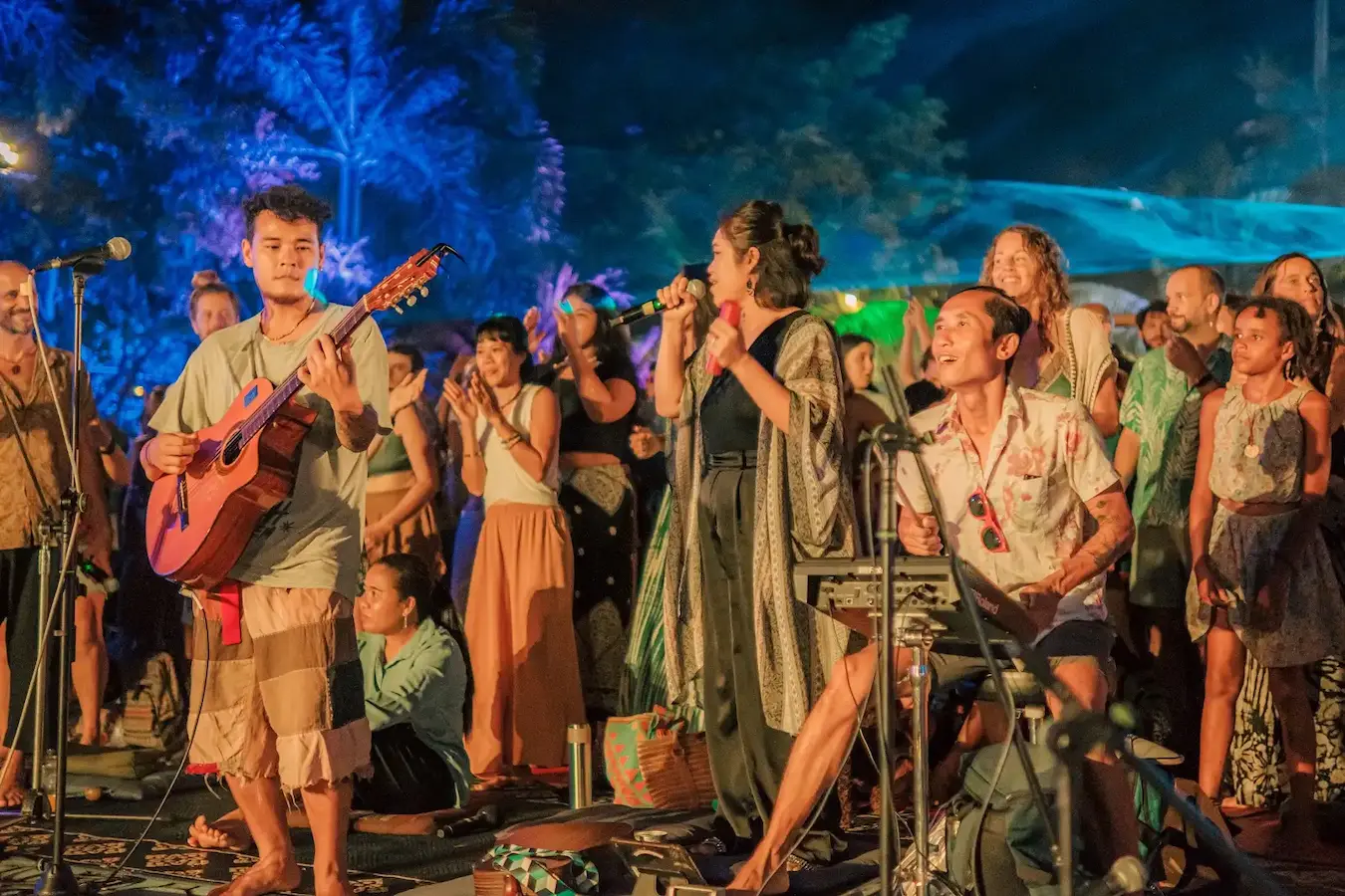 A guitarist and a singer lead a song while people stand and sing with them at night.