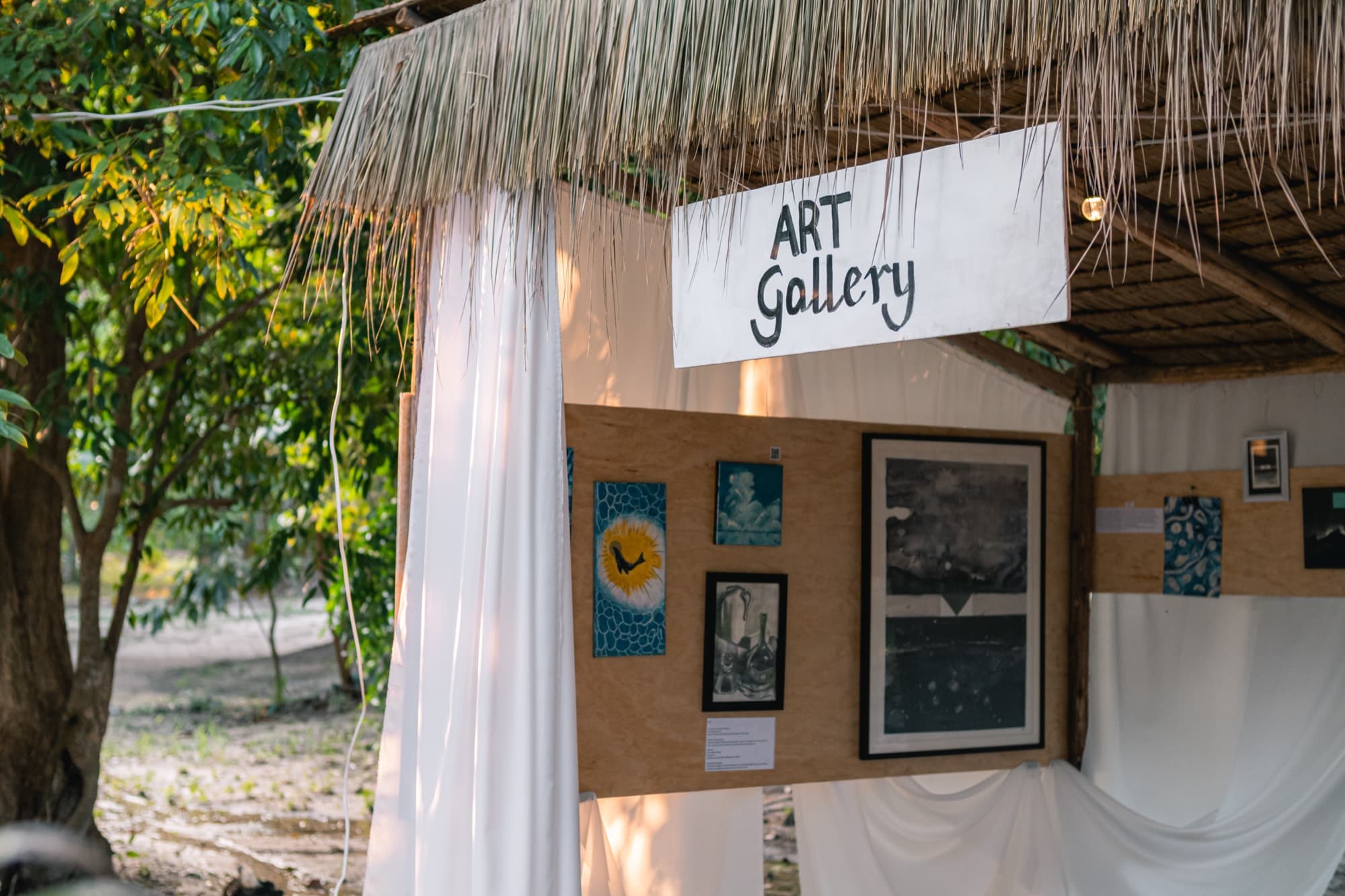 The Art Gallery booth at the Create Space, hung with framed work under a thatched roof