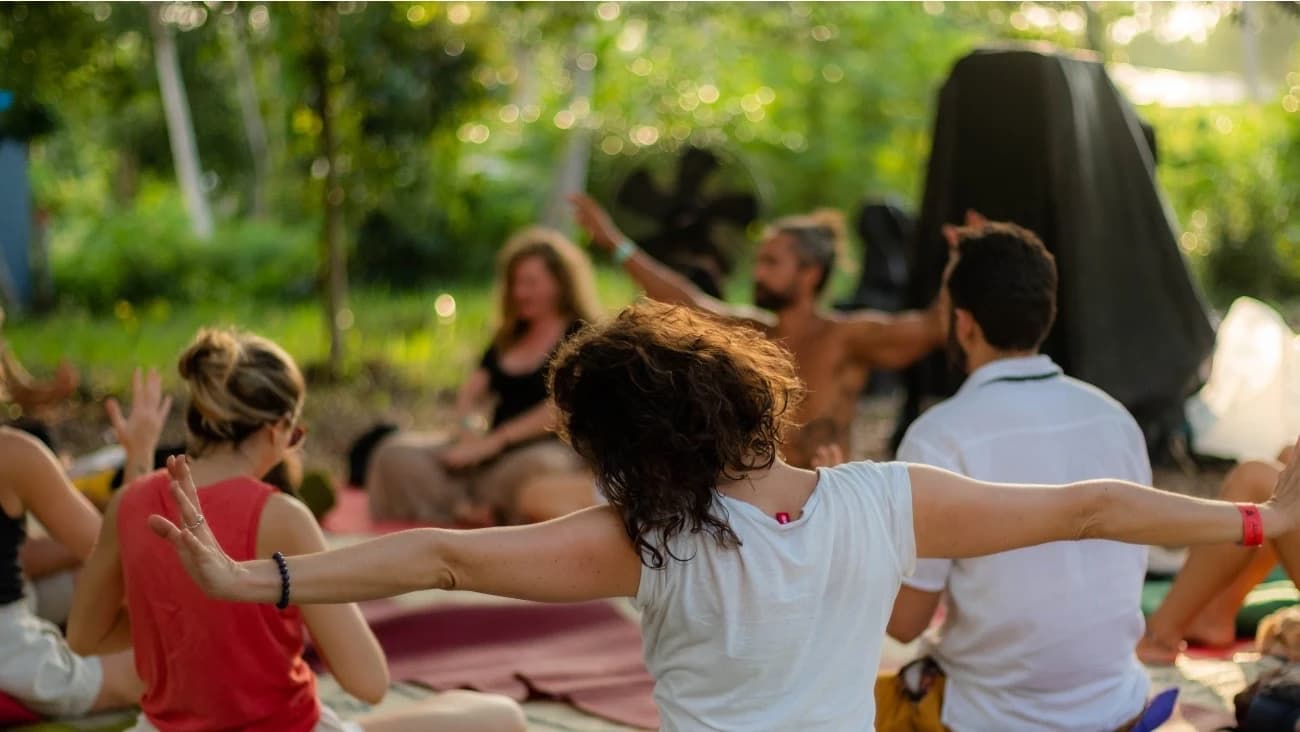A person seated on a mat opens both arms wide with the rest of the circle around them.