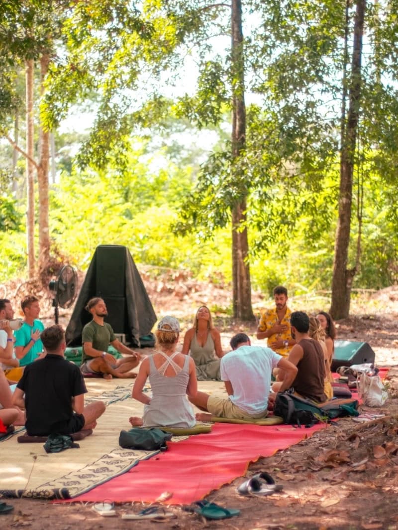 Woven mats and cushions laid out in a shaded clearing with people sitting on them.