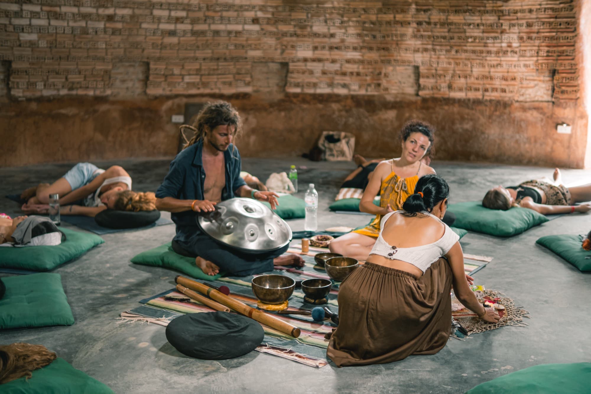 Two practitioners sit with a handpan, singing bowls and bamboo flutes on a rug inside the brick dome.