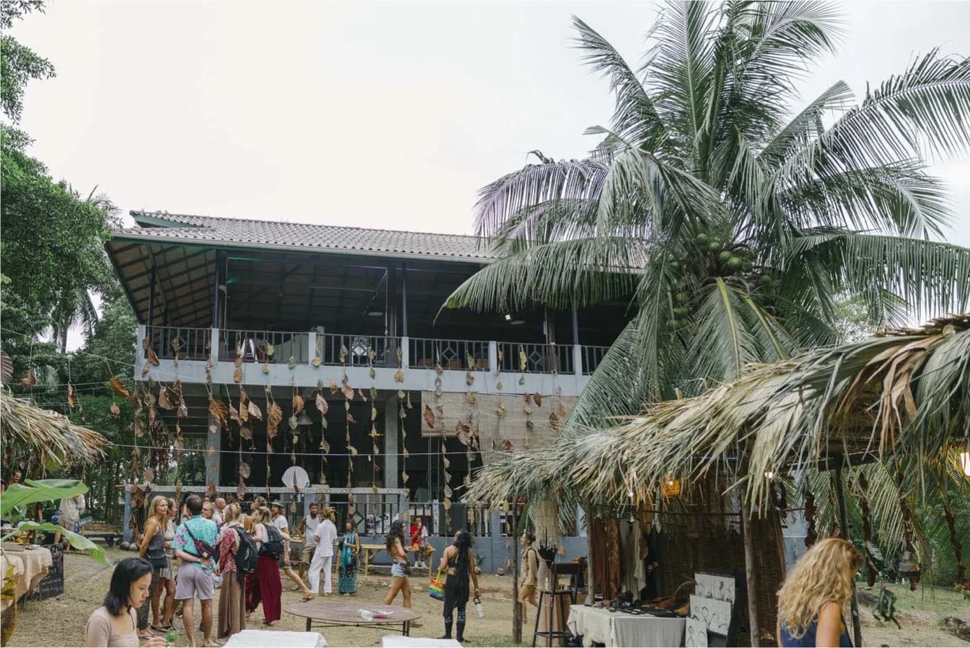 Market stalls under palm thatch on open ground in front of a two storey open sided building.