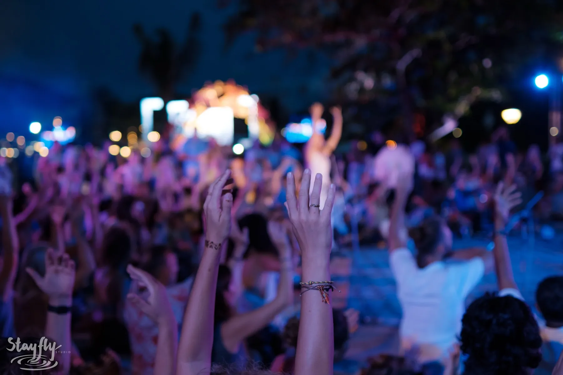 Hands raised in a crowd at night, lit blue from a stage out of focus behind them.
