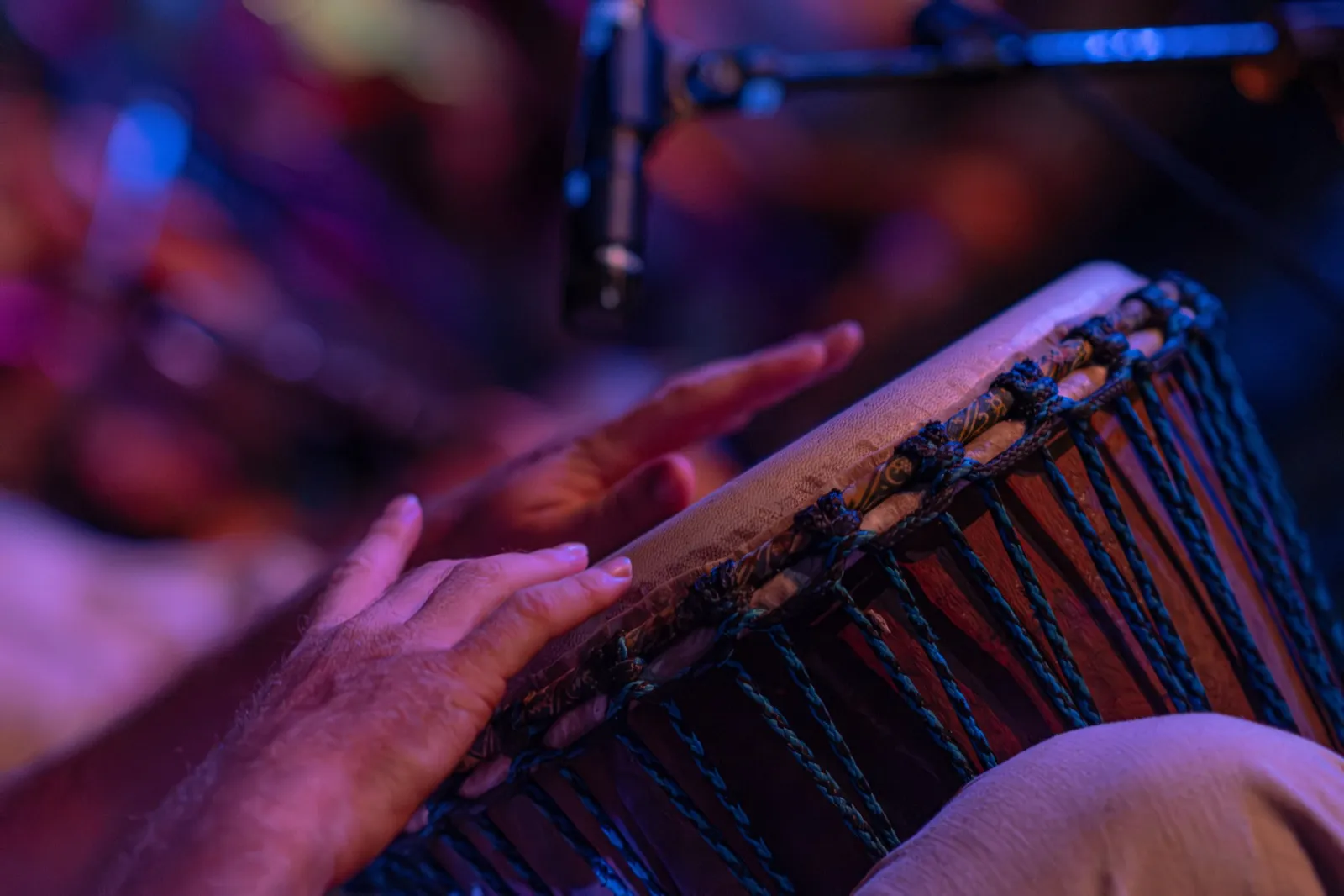 Two hands play a rope-tuned djembe beneath a microphone.