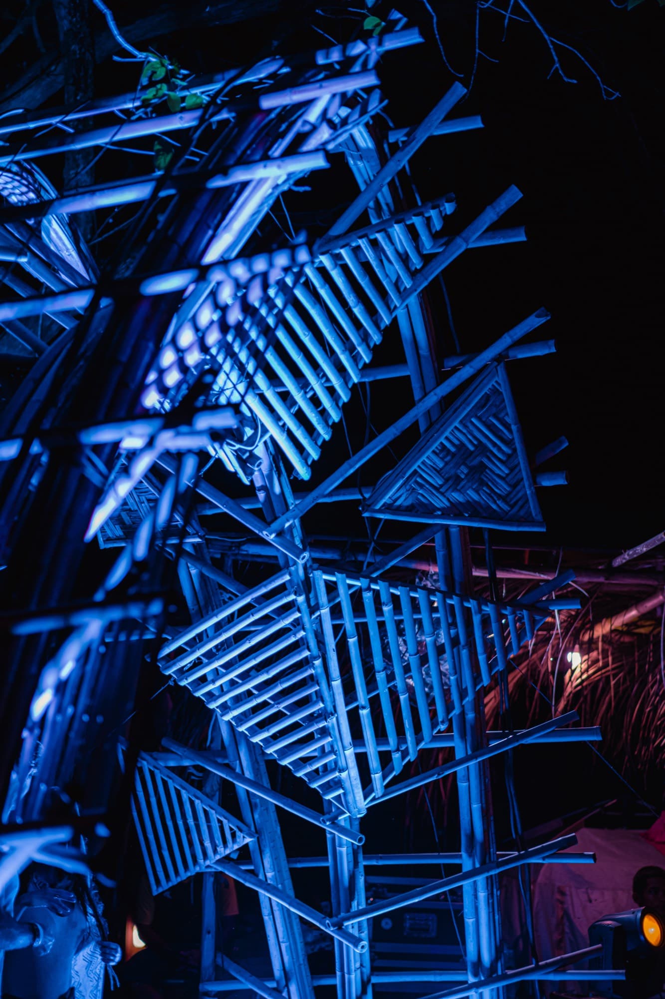 A bamboo sculpture lit blue against the night sky.
