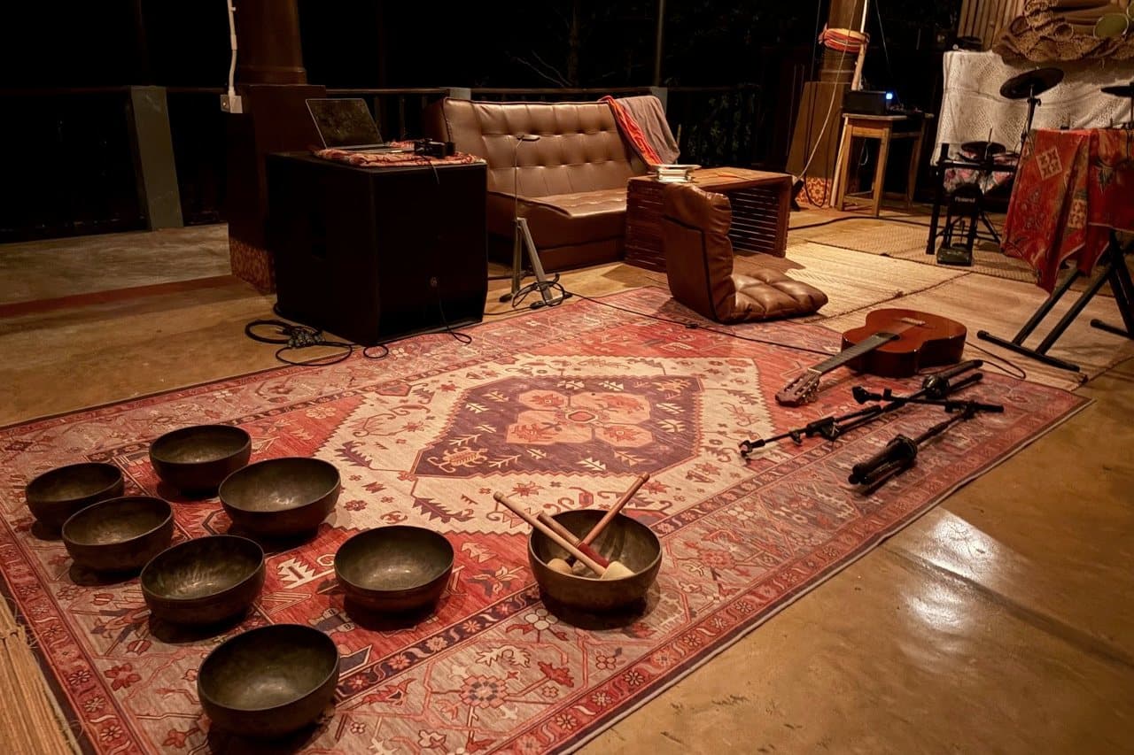 Singing bowls, a guitar and microphones rest on a patterned rug beside the Music Lounge seating area.