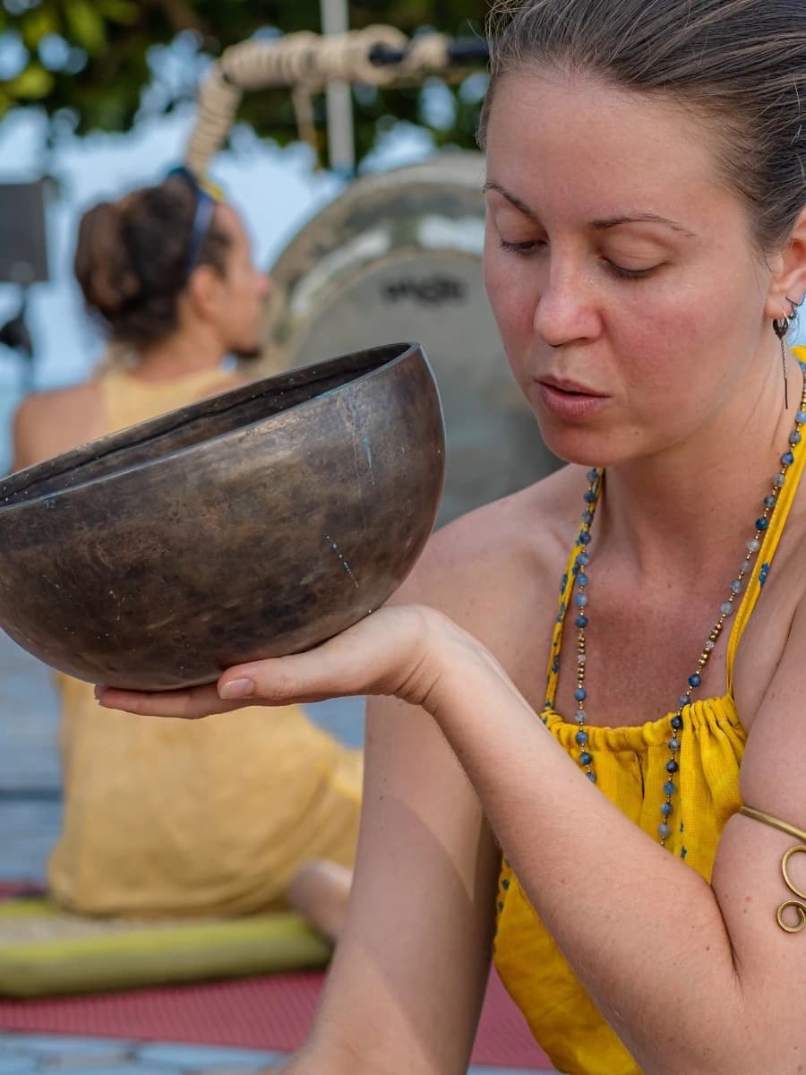 A woman holds a metal singing bowl balanced on her open palm.