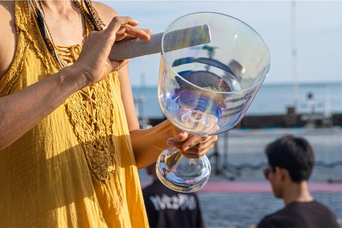 A person holds a crystal singing bowl in one hand and a striker in the other.