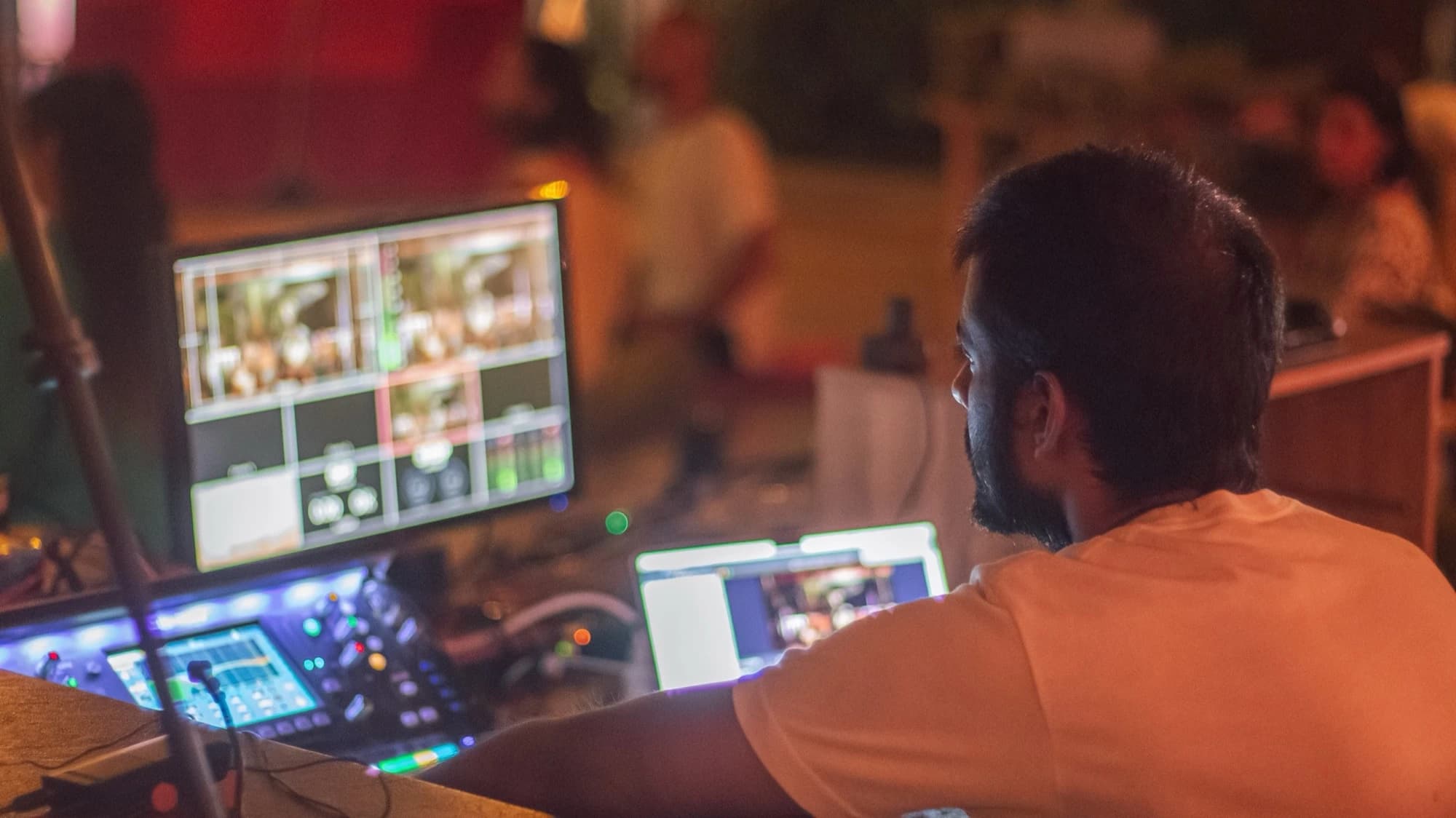 A multi view monitor, a video mixer and a laptop on an audio visual desk, with a technician working at the controls.