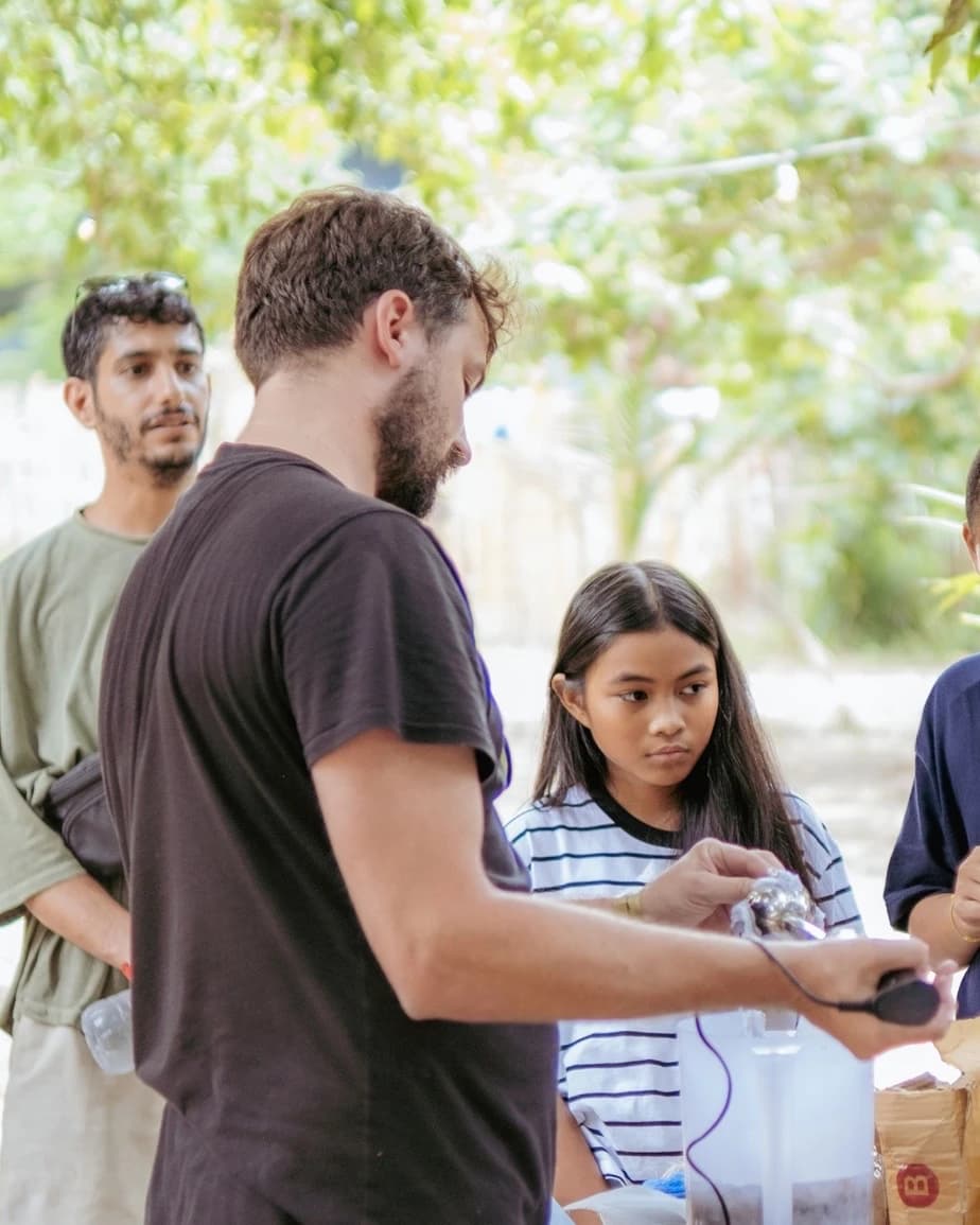 Someone demonstrating a hand tool at an outdoor table while young people watch closely