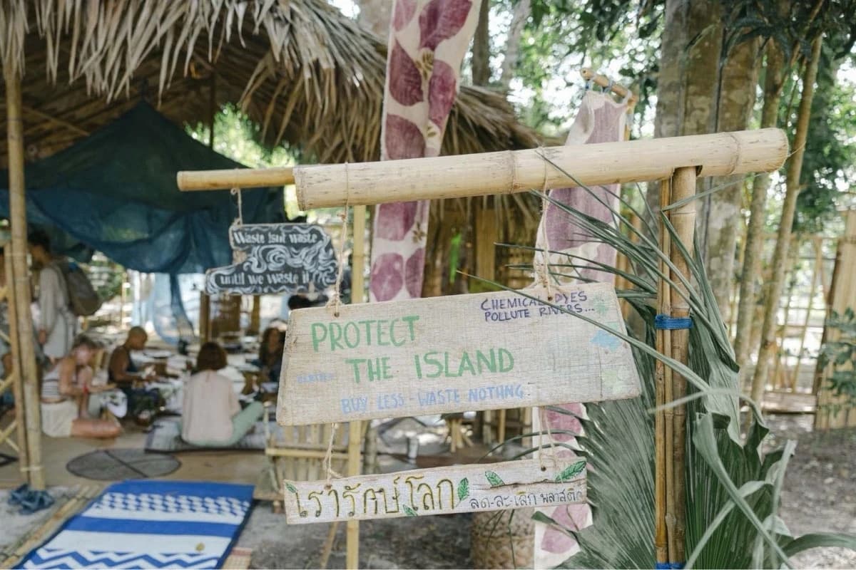 Hand painted wooden signs reading Protect the Island hang from a bamboo frame beside a thatched shelter.