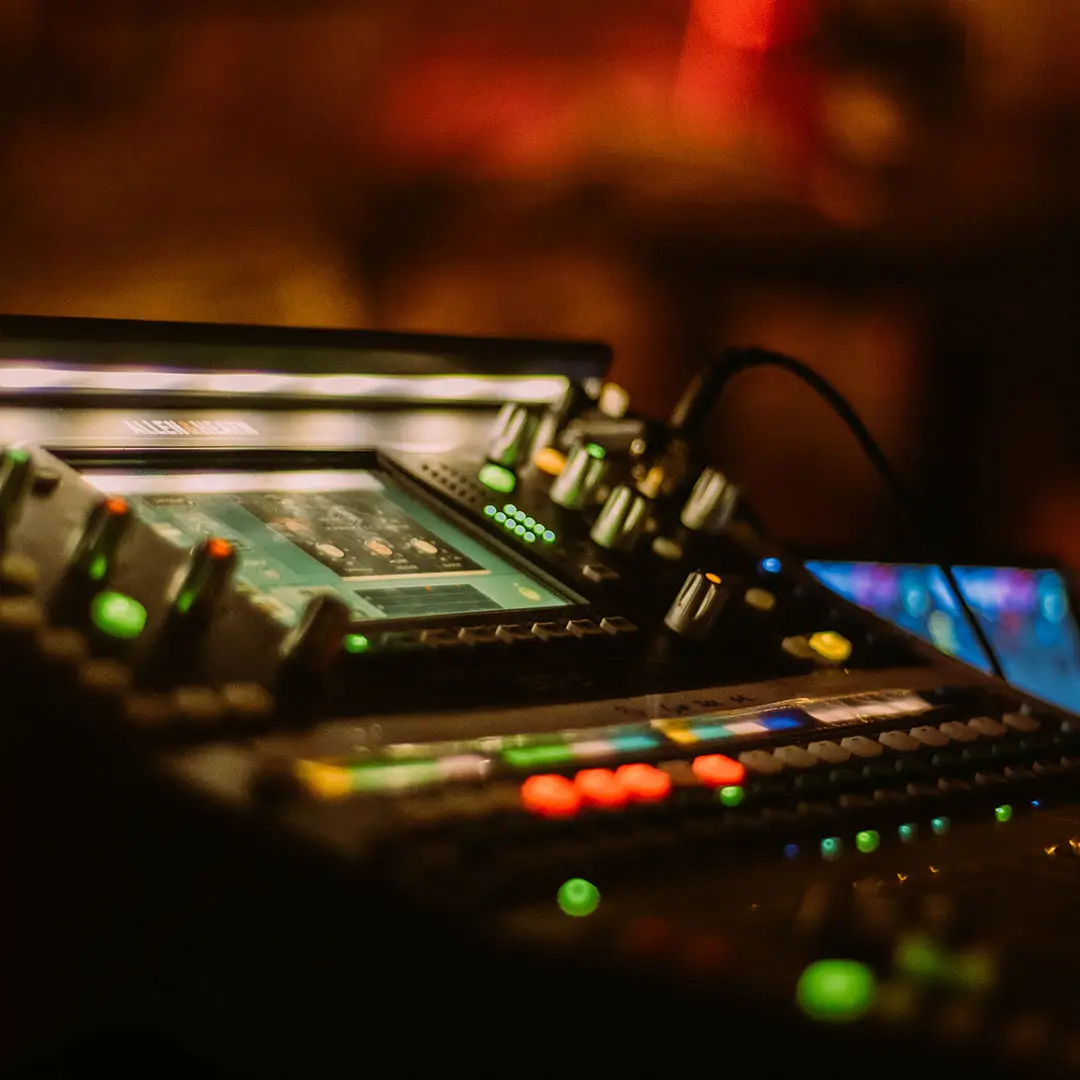 A digital mixing console lit with coloured lights in a dim room.