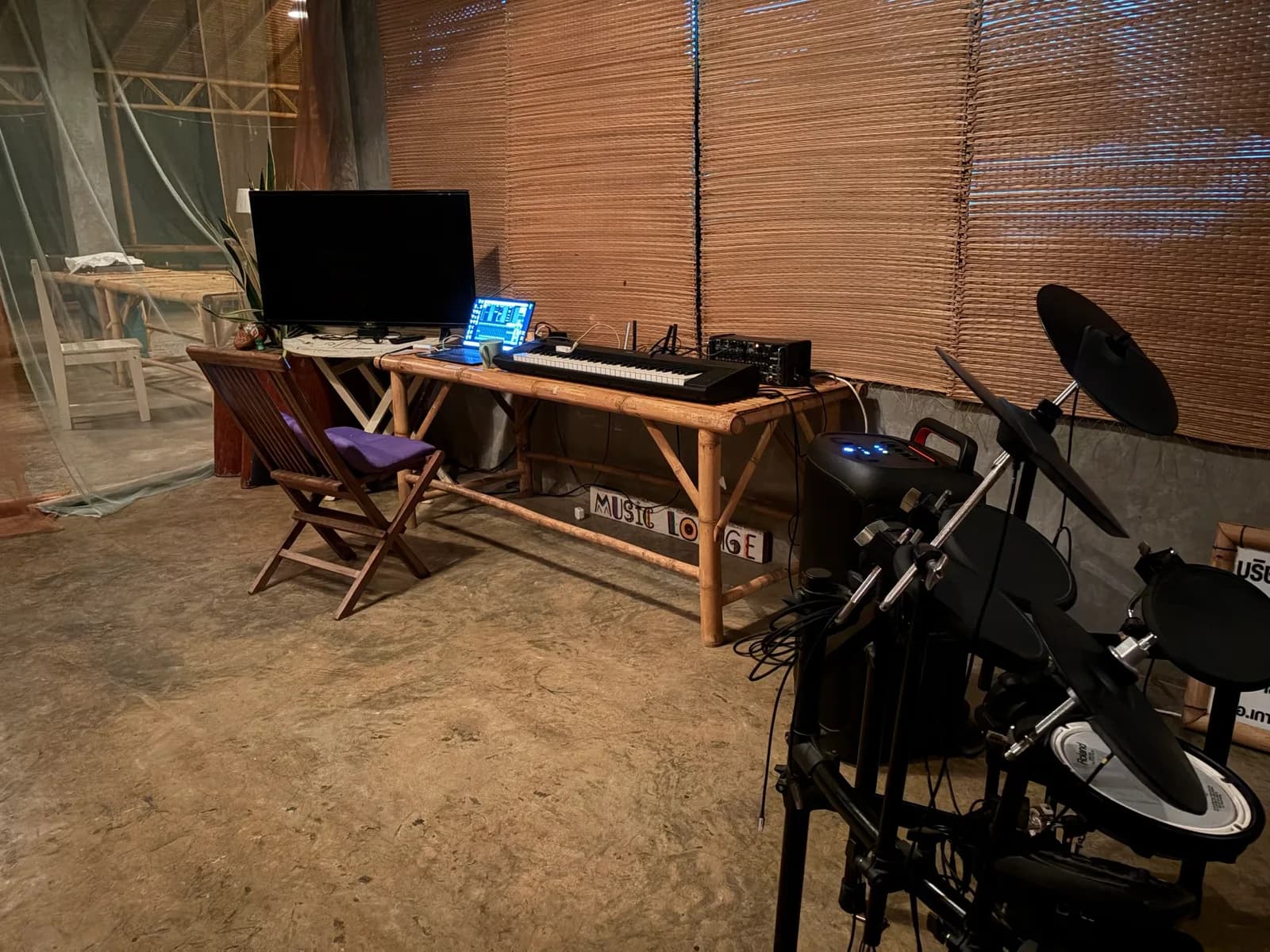 A bamboo desk with a laptop, monitor and keyboard beside the electronic drum kit in the rehearsal room.