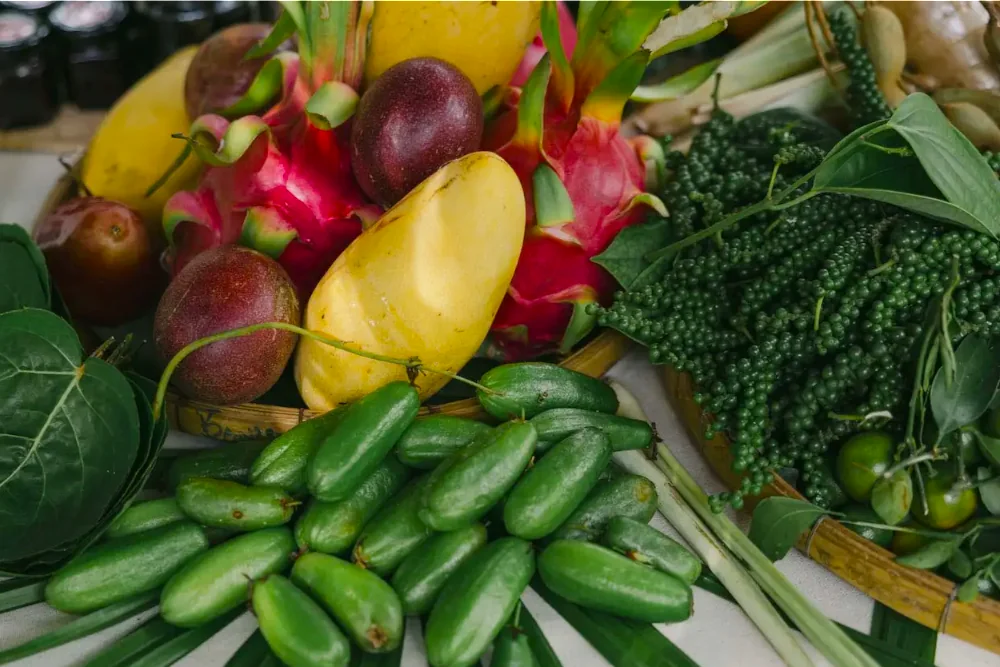 A harvest laid out on palm fronds: green cucumbers, clusters of fresh peppercorns, mango and dragon fruit.